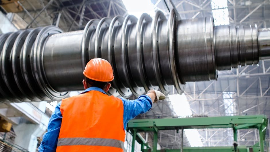 Engineer in high visibility vest and hard hat inspecting large machinery in factory setting.